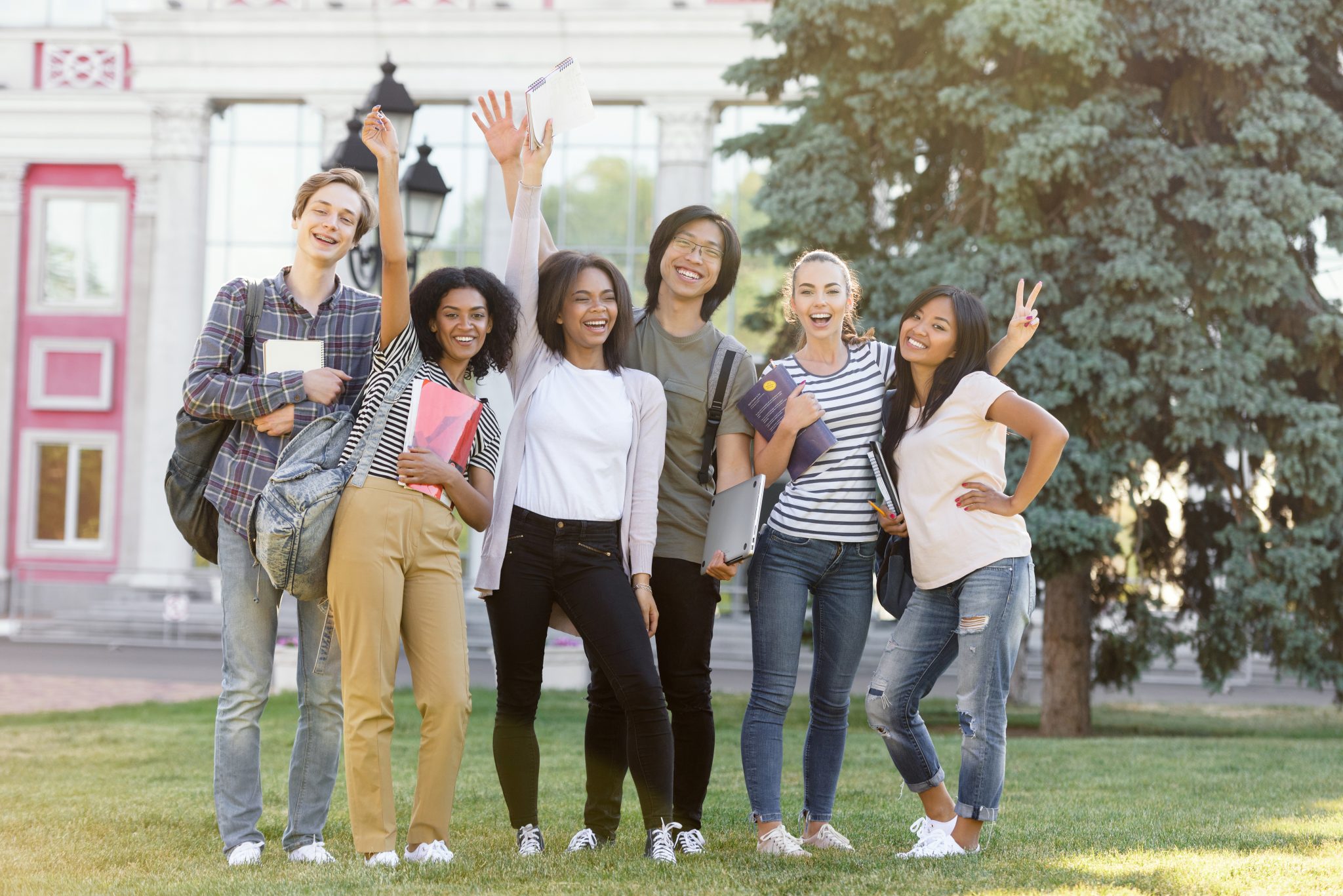 Image of multiethnic group of young cheerful students standing and waving outdoors. Looking at camera.